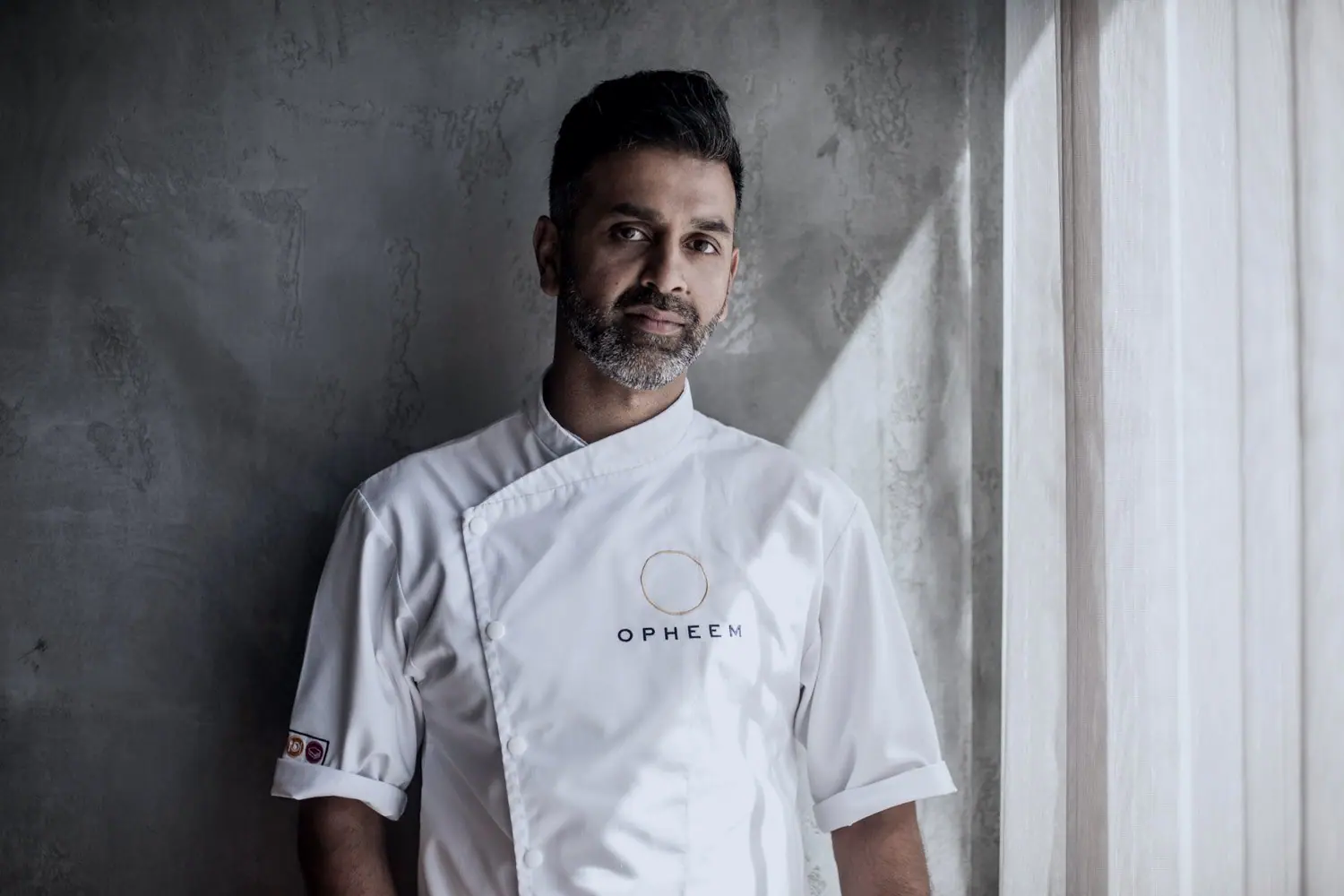 Aktar Islam in chef's whites, leaning against a concrete wall