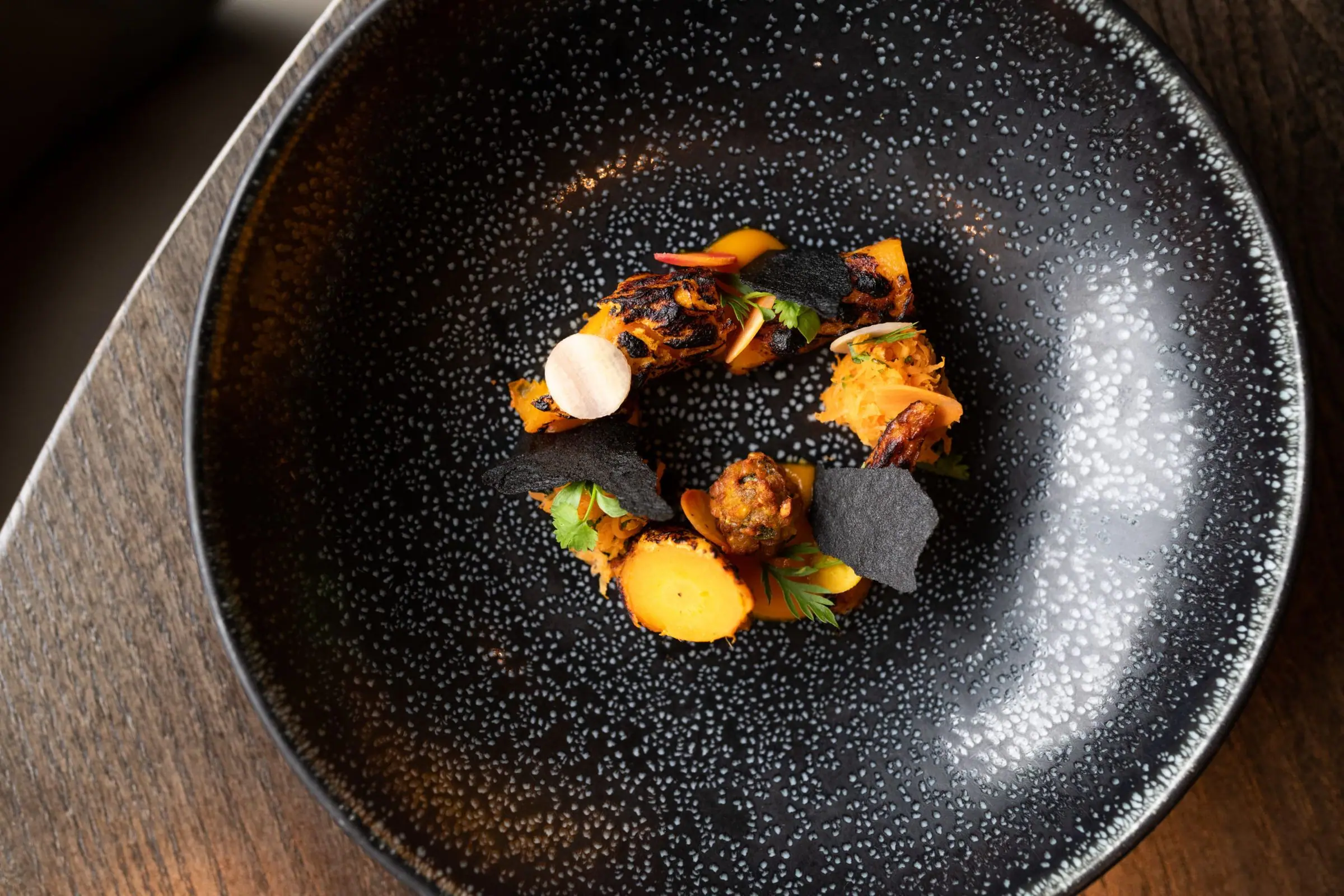 Crisp fried morsels and roasted roots on a speckled black plate