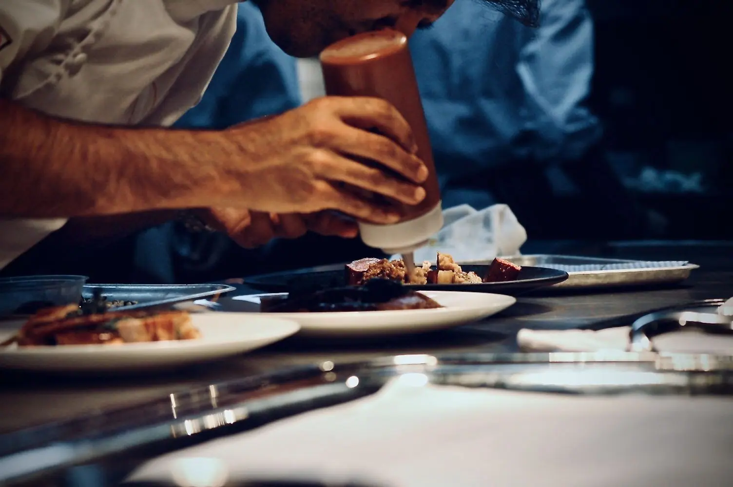 A chef's hands piping onto a row of plates