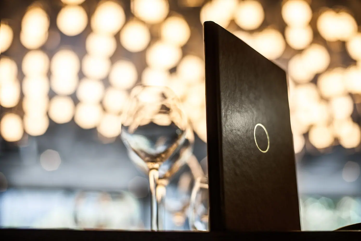The Opheem menu folder, marked with the gold ring, standing on a table under the dining room lights