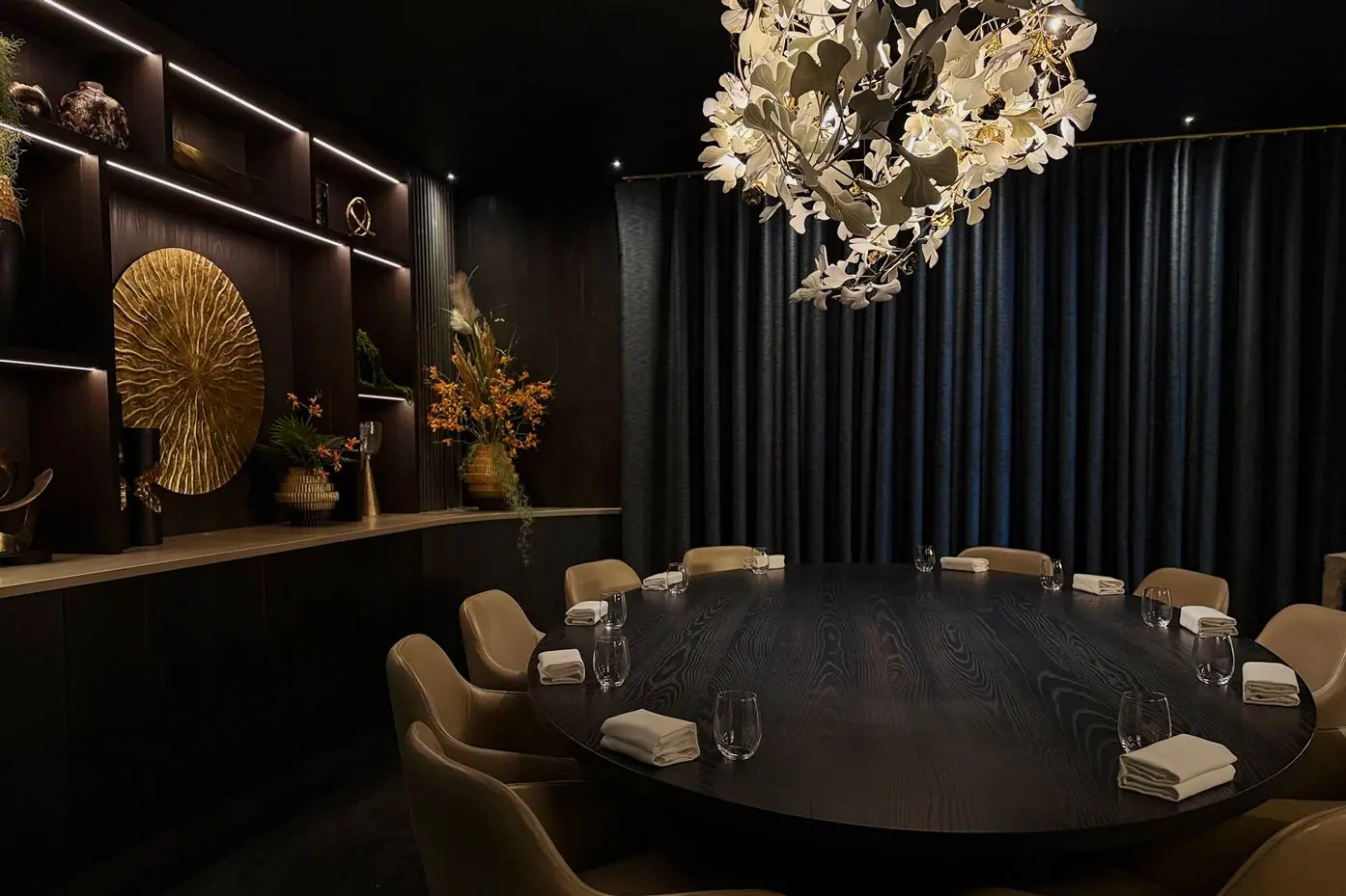 The oval table laid for dinner, with the dark wood shelves and the leaf canopy above