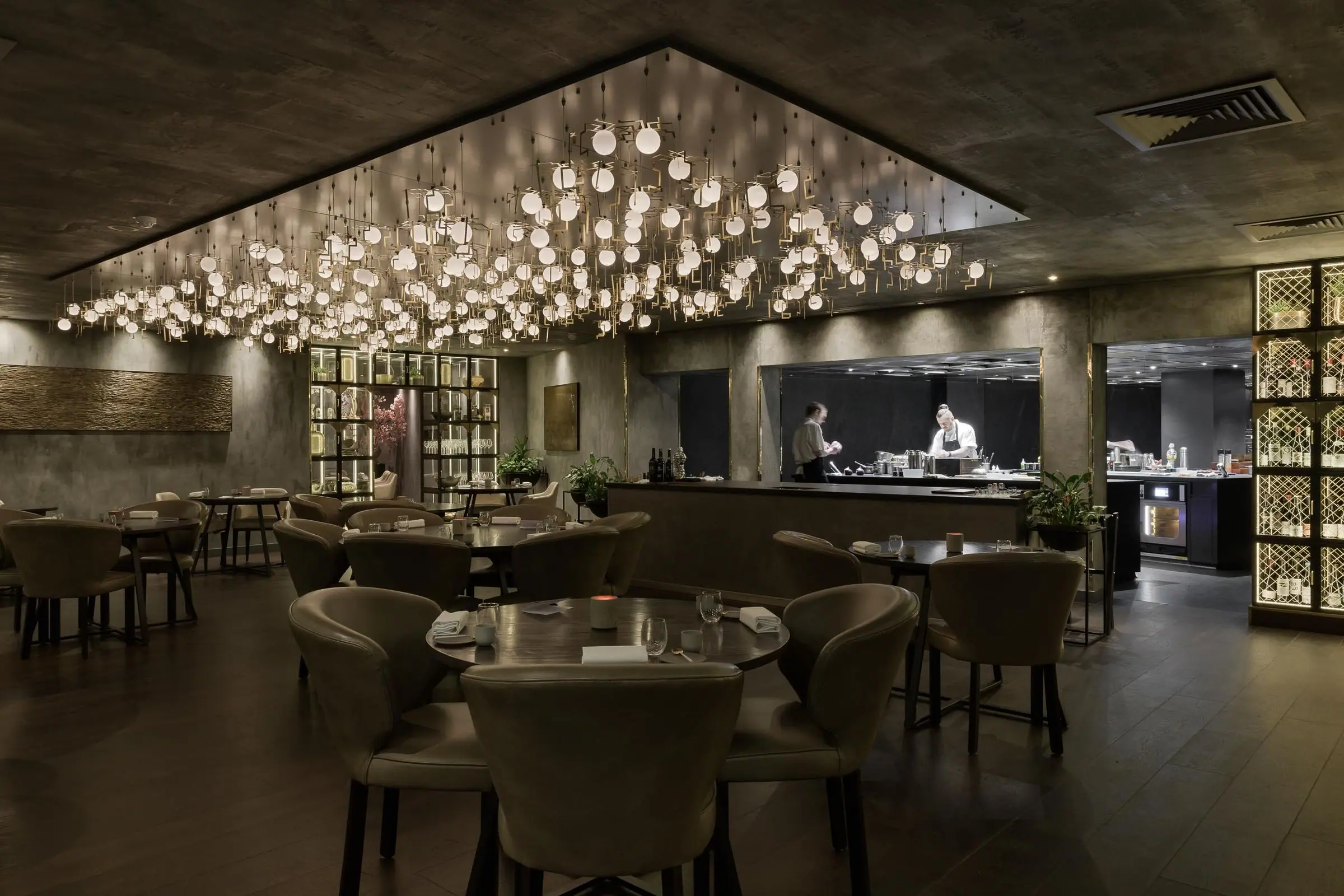 The Opheem dining room under its ceiling of hanging lights, with the open kitchen at the back